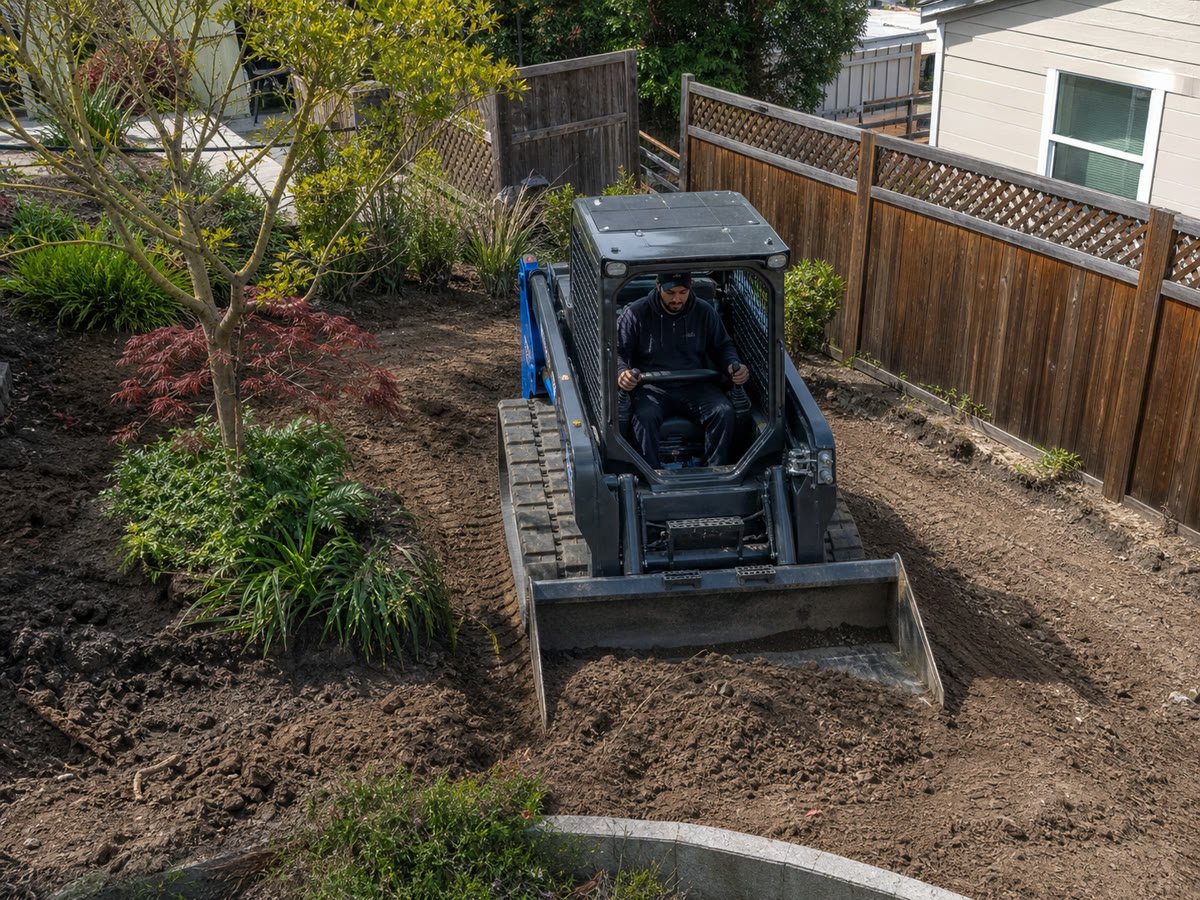 Compact track loader working precisely in a tight fenced backyard