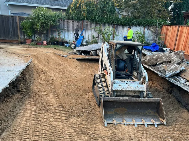 Skid steer grading a backyard down to bare dirt after demolition
