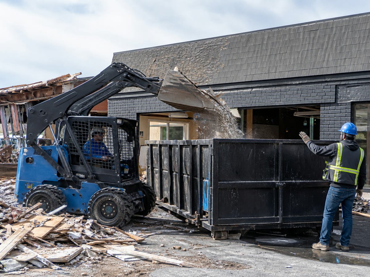 Skid steer loading storefront debris into a roll off container