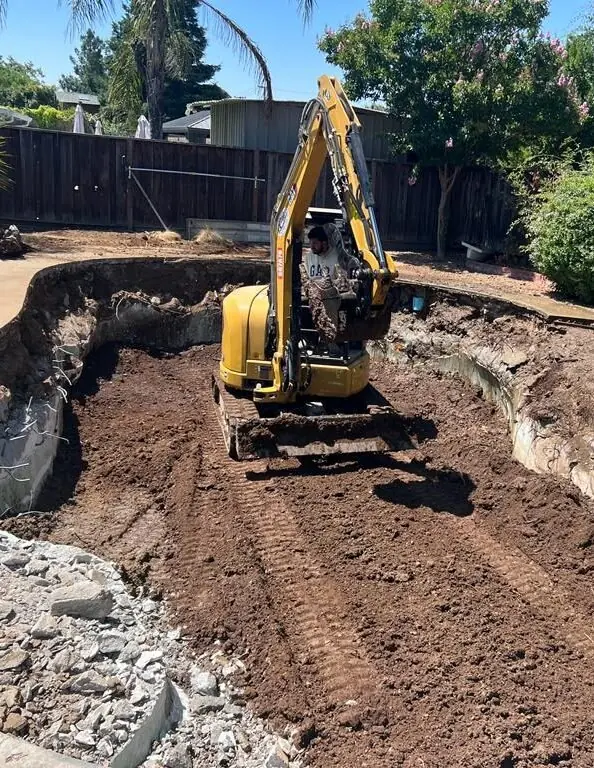 Excavator breaking out an old gunite swimming pool shell in a Contra Costa County backyard