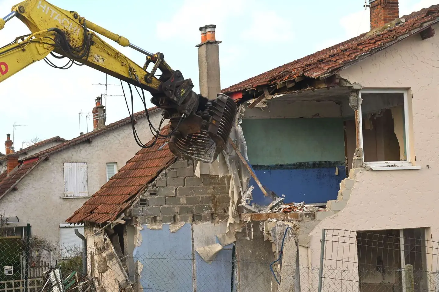 Excavator tearing into the roofline of a house during demolition