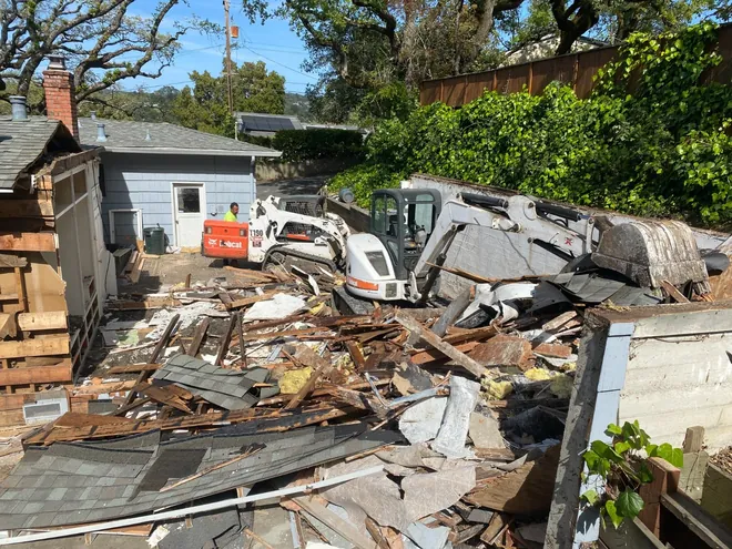 Residential teardown with debris pile, skid steer and roll-off container